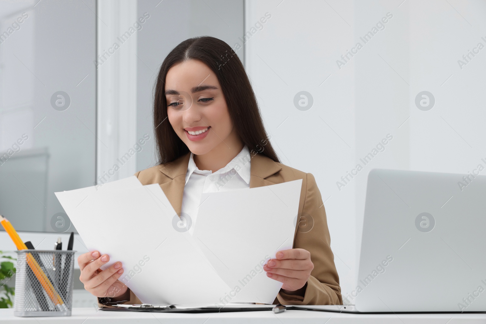 Photo of Young female intern working with laptop at table in office