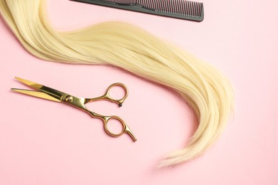 Professional hairdresser scissors and comb with blonde hair strand on pink background, top view