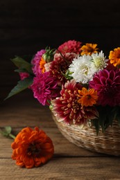 Photo of Beautiful wild flowers and leaves in wicker basket on wooden table, closeup