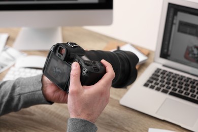 Photo of Professional photographer with digital camera at wooden table indoors, closeup