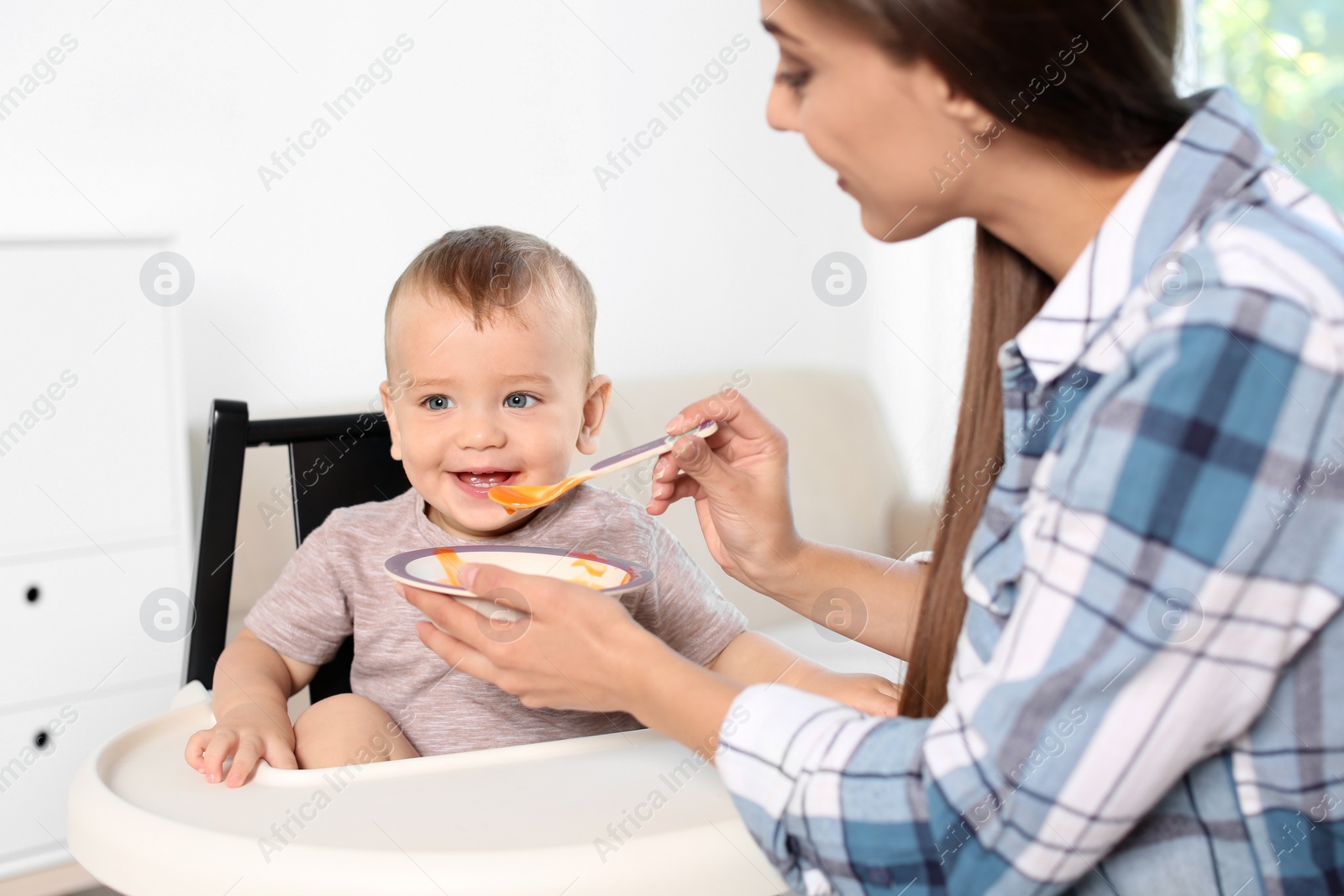 Photo of Woman feeding her child in highchair indoors. Healthy baby food