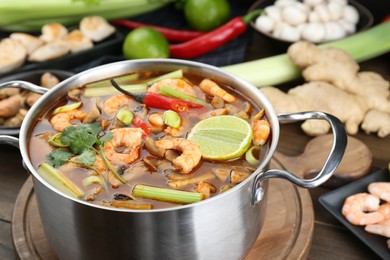 Photo of Saucepan with delicious Tom Yum soup and ingredients on table, closeup