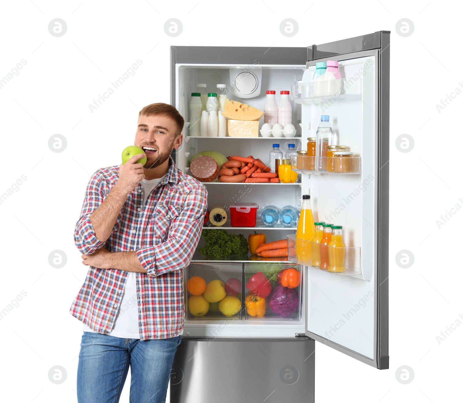 Photo of Young man eating apple near open refrigerator on white background