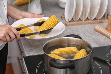 Photo of Woman putting raw corn cob into stewpot on stove, closeup