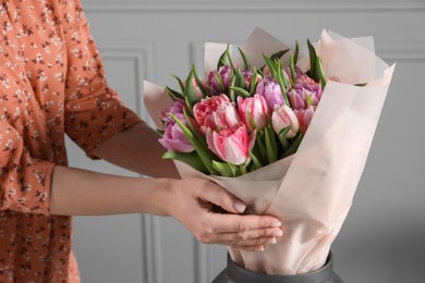 Photo of Woman putting bouquet of beautiful tulips in vase indoors, closeup