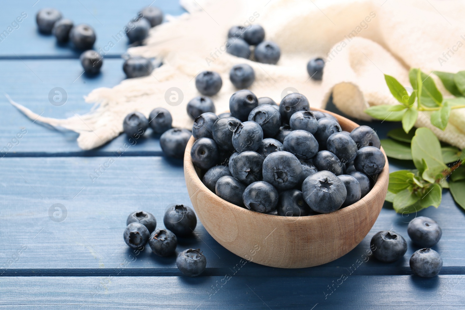 Photo of Tasty fresh blueberries and green leaves on blue wooden table, closeup