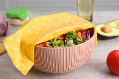 Photo of Bowl of fresh salad covered with beeswax food wrap on light grey table in kitchen