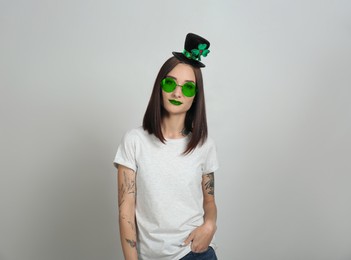 Image of St. Patrick's day party. Pretty woman in leprechaun hat and green sunglasses on light grey background
