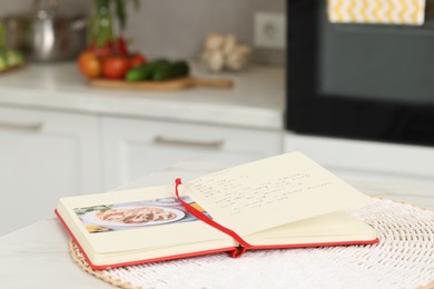 Recipe book on white marble table in kitchen, closeup. Space for text