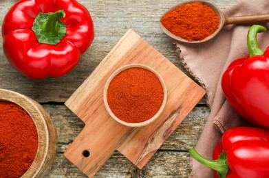 Photo of Bowls, spoon with aromatic paprika powder and fresh bell peppers on old wooden table, flat lay