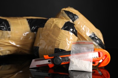 Photo of Smuggling, drug trafficking. Packages with narcotics and utility knife on black mirror surface, closeup