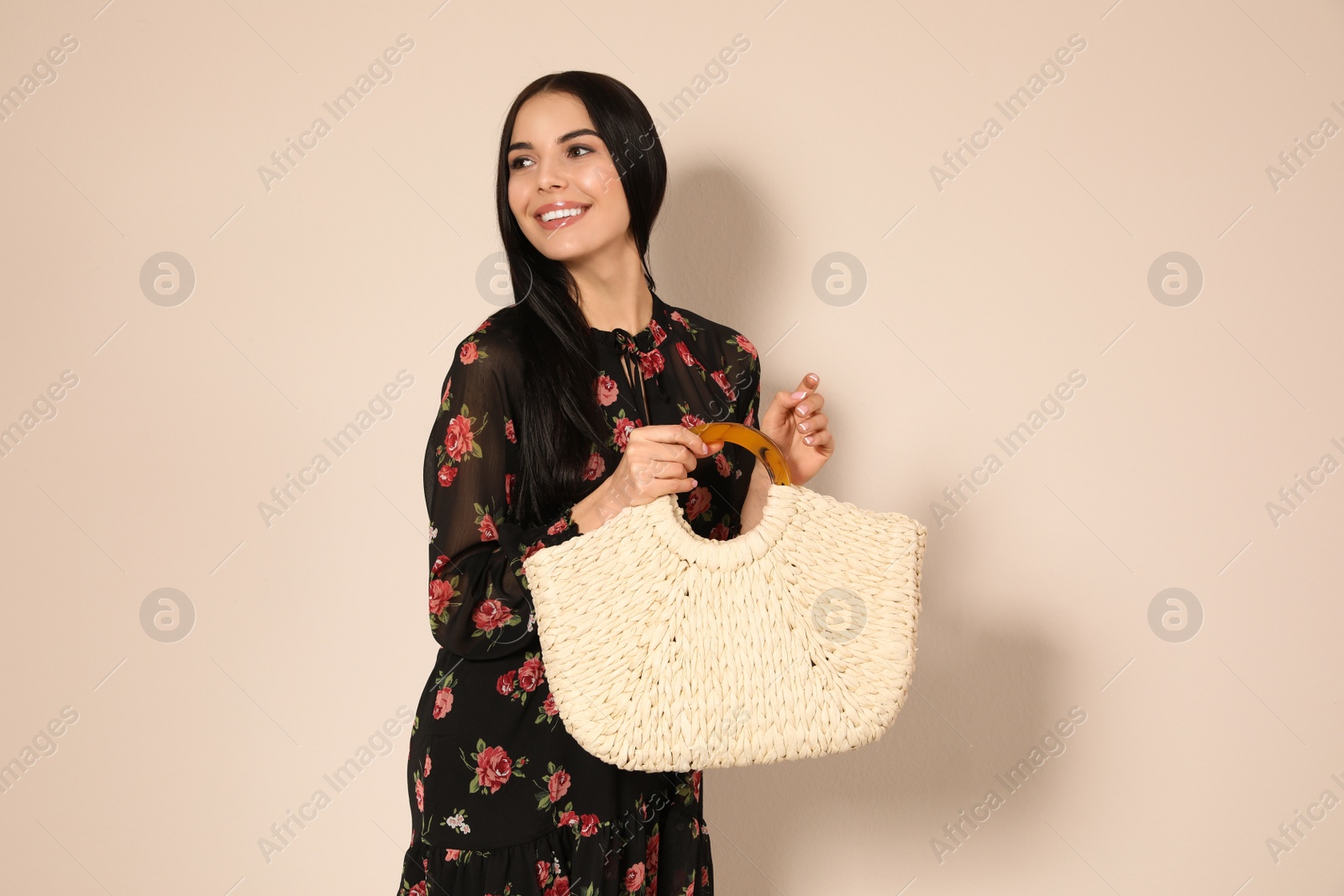 Photo of Young woman wearing floral print dress with straw bag on beige background