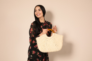 Photo of Young woman wearing floral print dress with straw bag on beige background