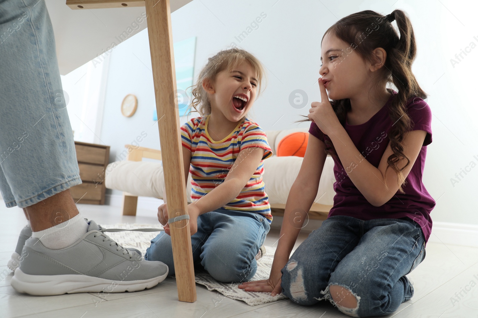 Photo of Cute little children tying shoe laces of their father together at home, closeup