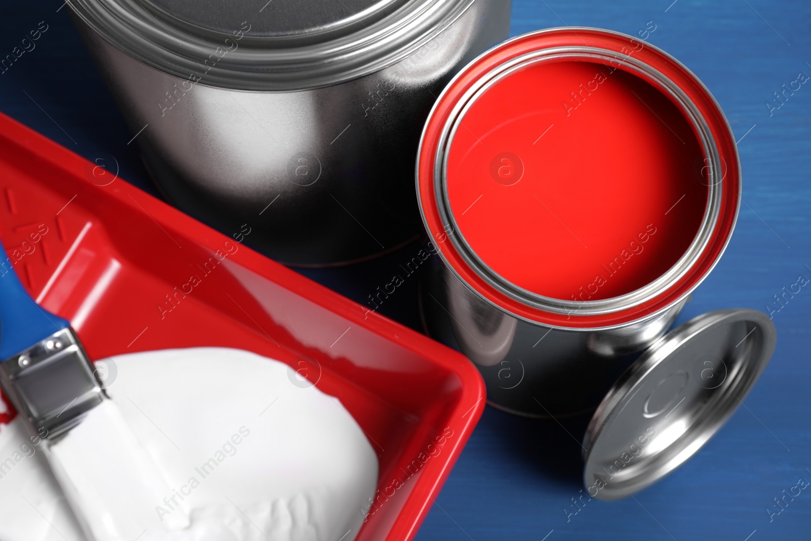 Photo of Cans of paints, brush and tray on blue wooden background, closeup