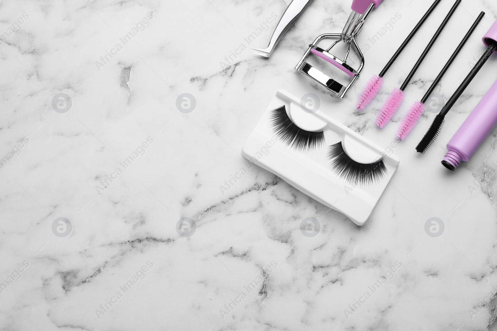 Photo of Flat lay composition with false eyelashes and tools on white marble table. Space for text