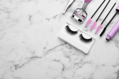 Flat lay composition with false eyelashes and tools on white marble table. Space for text