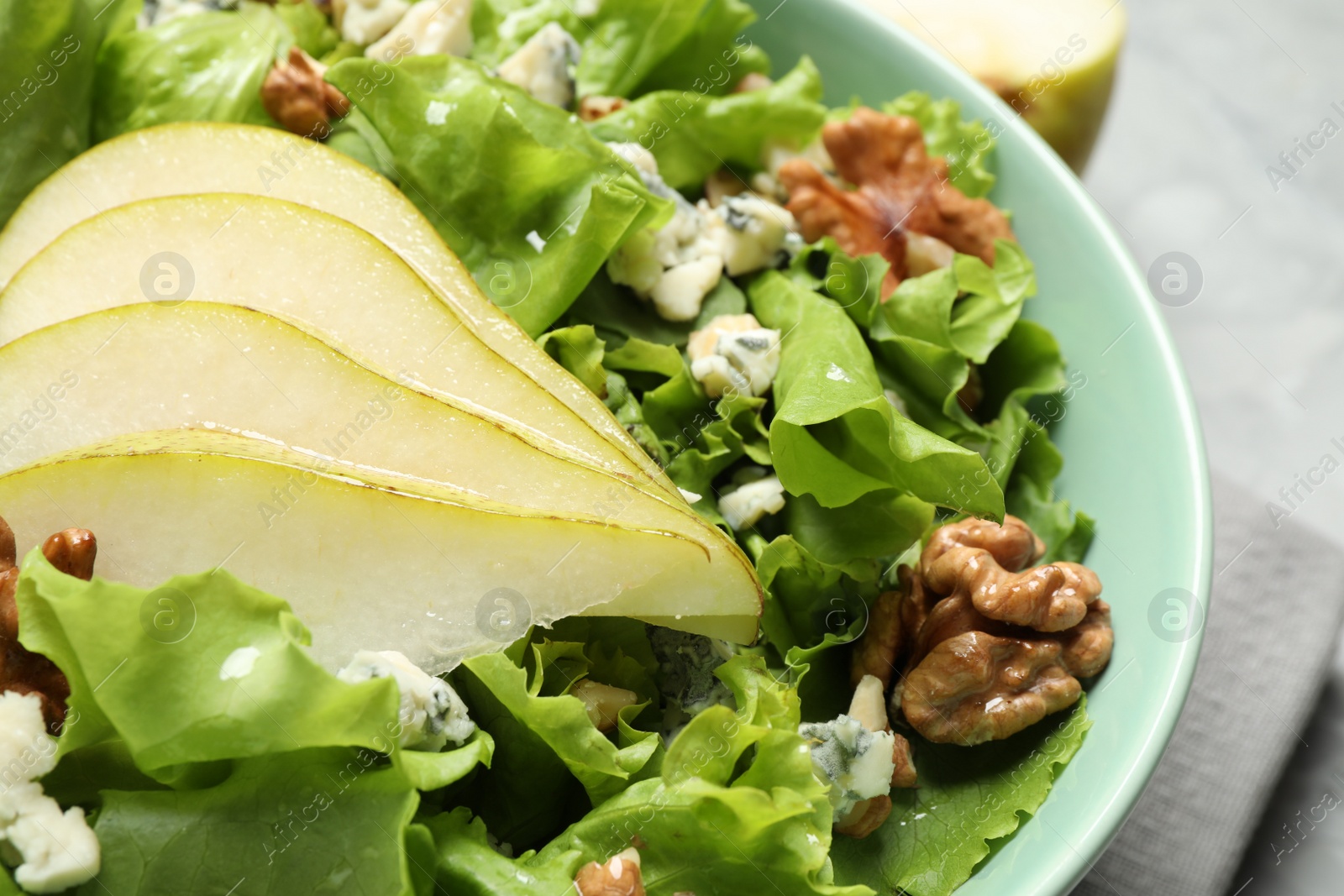 Photo of Tasty salad with pear slices, lettuce and walnuts in bowl, closeup