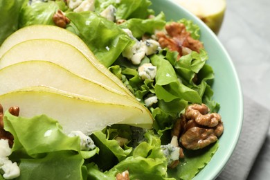 Tasty salad with pear slices, lettuce and walnuts in bowl, closeup