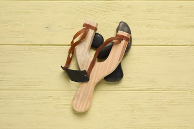 Slingshot with stones on yellow wooden background, top view