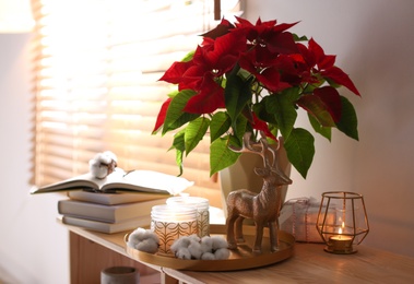 Beautiful poinsettia, burning candles and decorative deer on wooden rack indoors, space for text. Traditional Christmas flower