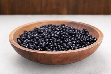 Photo of Bowl of raw black beans on light grey table, closeup