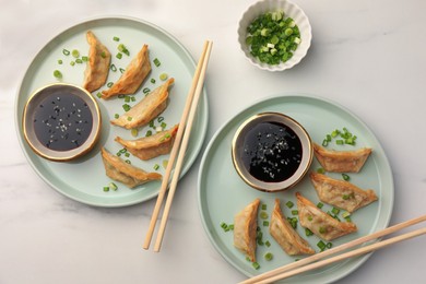 Photo of Delicious gyoza (asian dumplings) with soy sauce, green onions and chopsticks on white table, flat lay