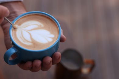 Photo of Barista creating pattern in cup of coffee on blurred background, closeup. Space for text