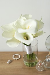 Beautiful calla lily flowers in glass vase, bottles with perfumes, jewelry and mirror on wooden table