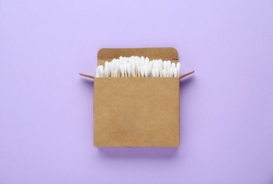 Photo of Box with wooden cotton buds on violet background, top view