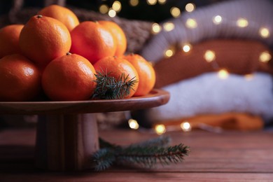 Stand with delicious ripe tangerines and fir twigs on wooden table. Space for text