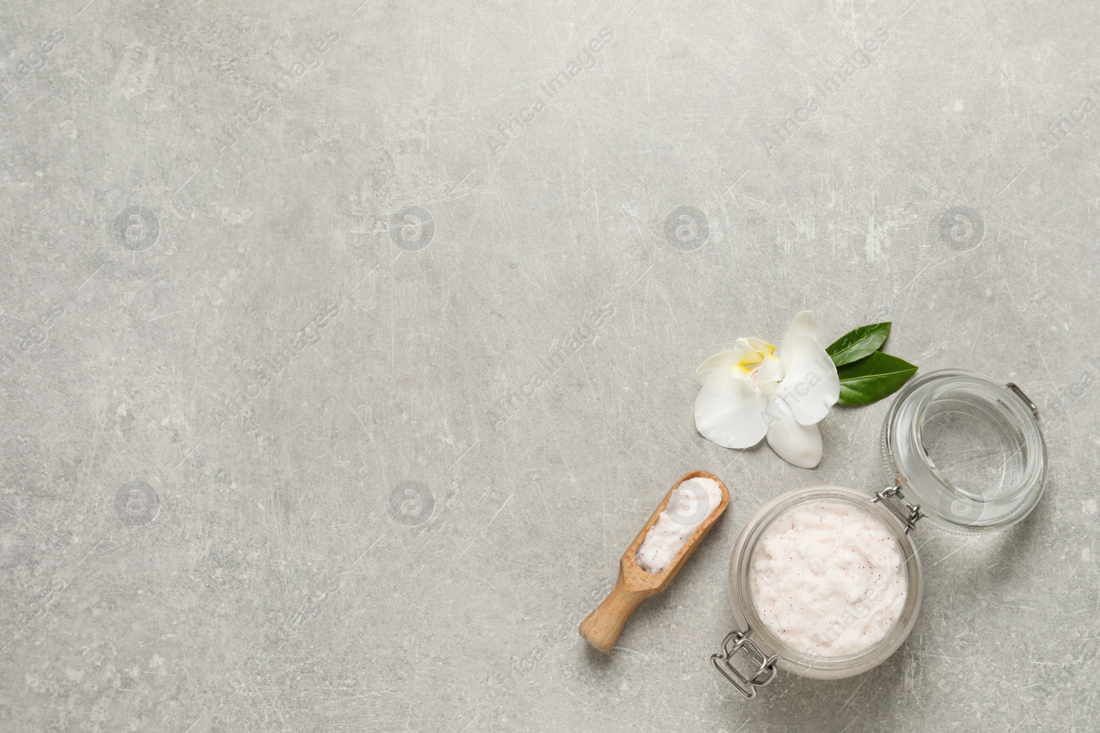 Photo of Body scrub in glass jar and scoop near orchid flower on light grey table, flat lay. Space for text