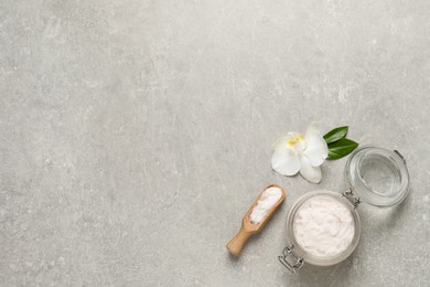 Photo of Body scrub in glass jar and scoop near orchid flower on light grey table, flat lay. Space for text