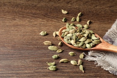 Photo of Spoon with dry cardamom pods on wooden table, space for text