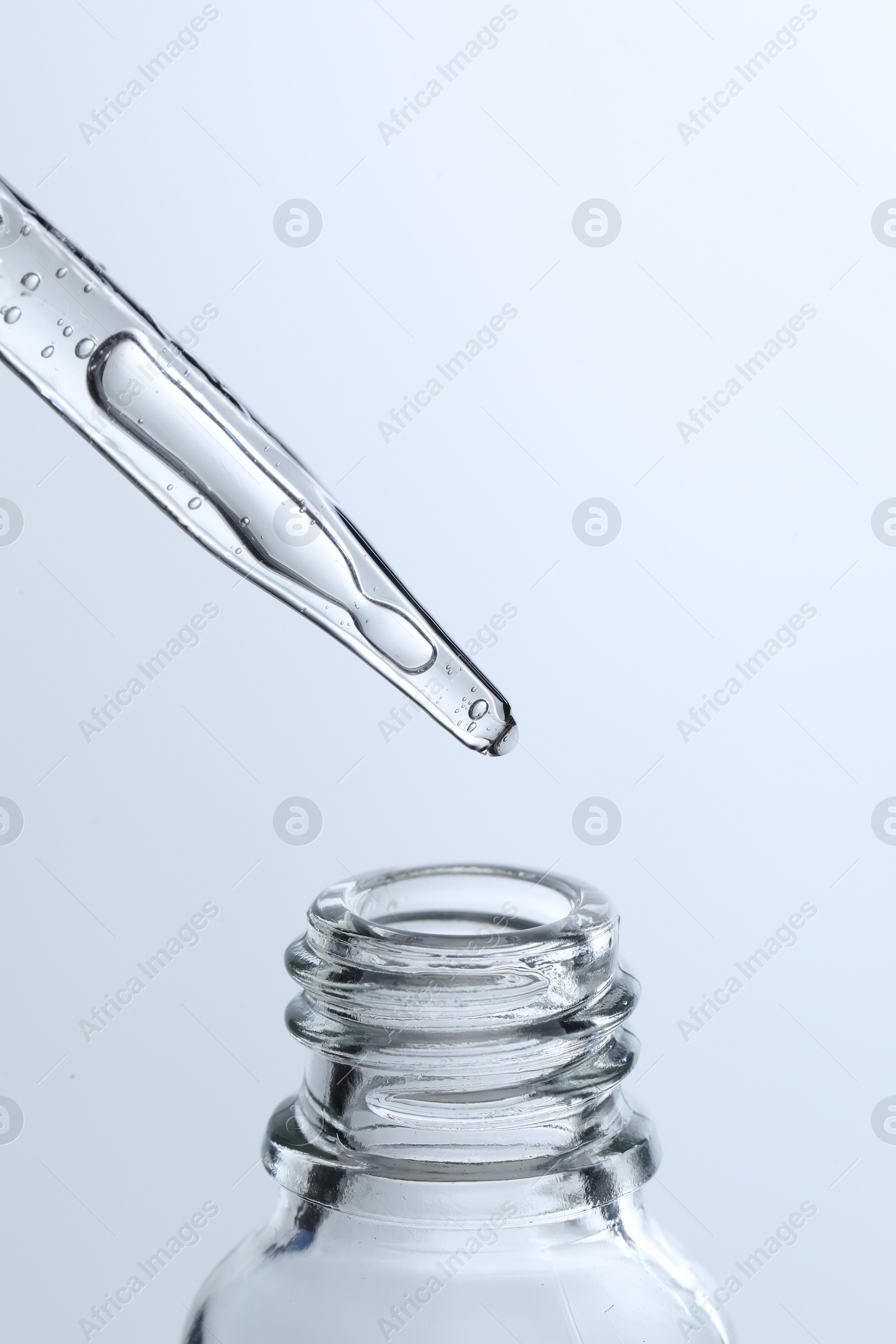 Photo of Dripping liquid from pipette into glass bottle on light blue background, closeup