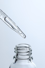 Dripping liquid from pipette into glass bottle on light blue background, closeup