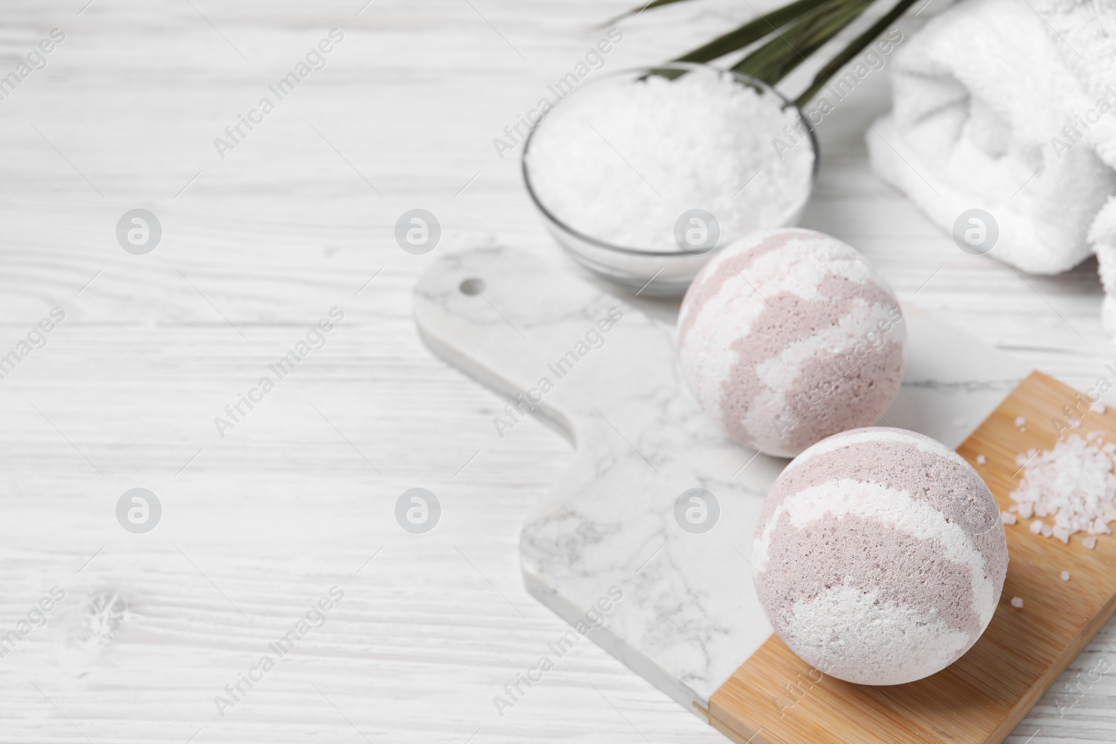 Photo of Bath bombs, sea salt and rolled towel on white wooden table, space for text