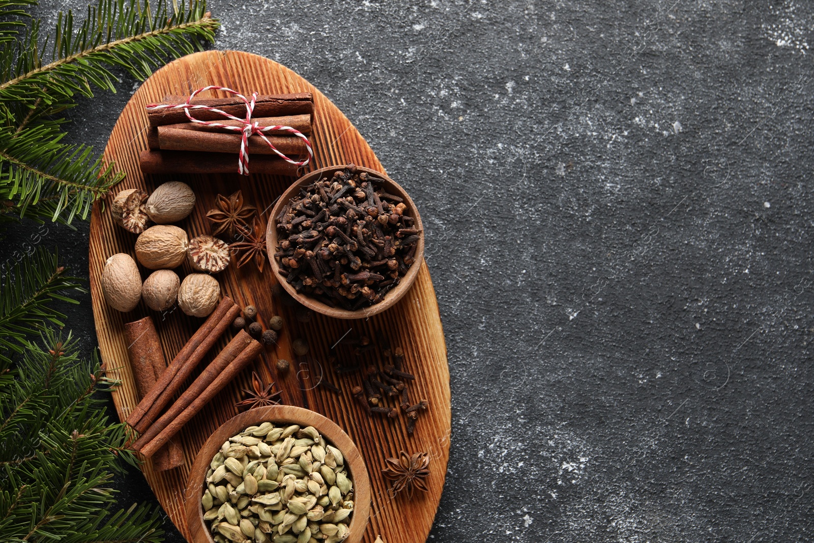 Photo of Different spices and fir branches on dark gray table, flat lay. Space for text