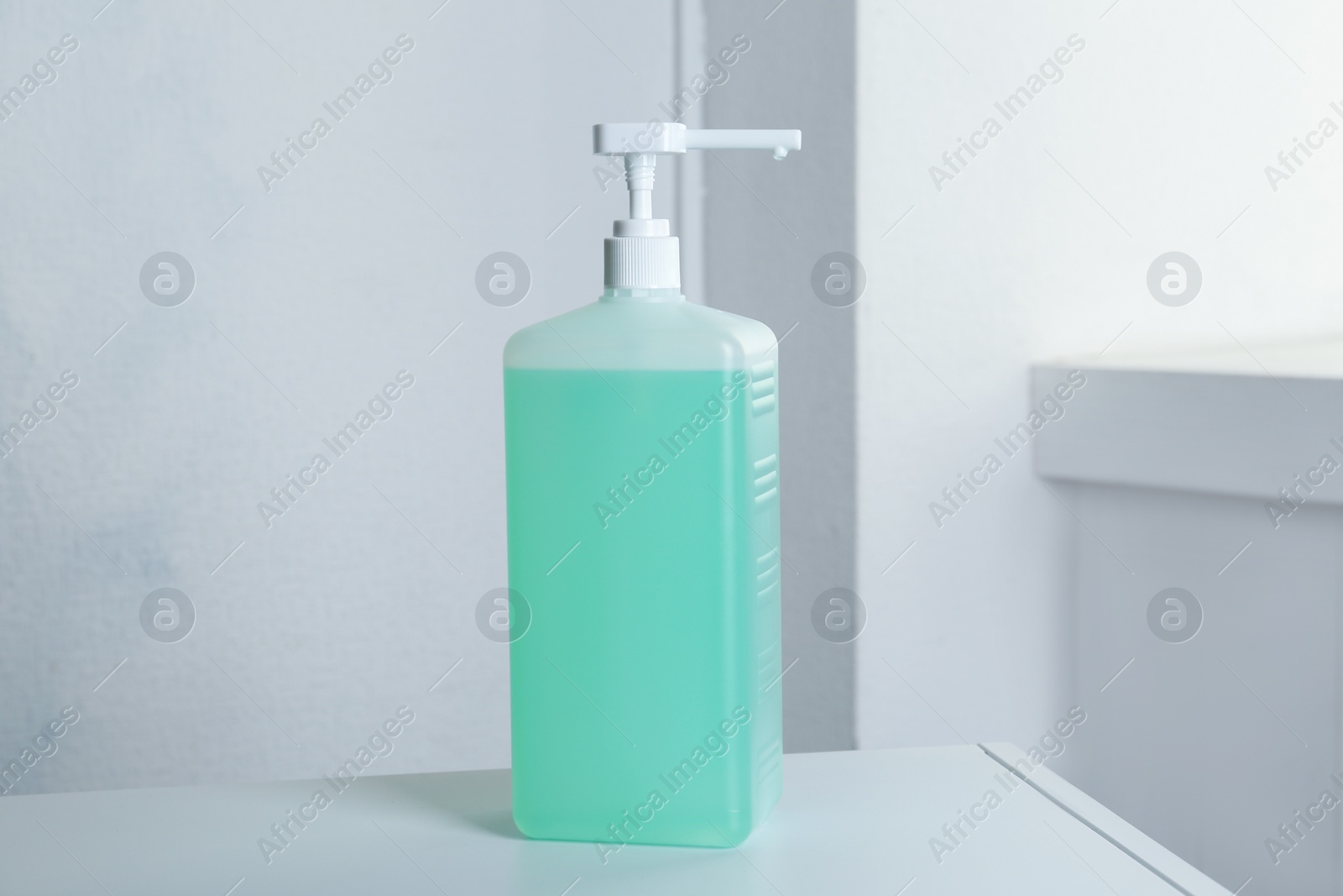 Photo of Dispenser bottle with green antiseptic gel on table indoors