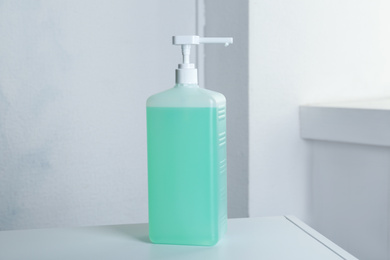 Photo of Dispenser bottle with green antiseptic gel on table indoors