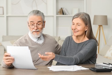 Elderly couple with papers discussing pension plan at wooden table indoors