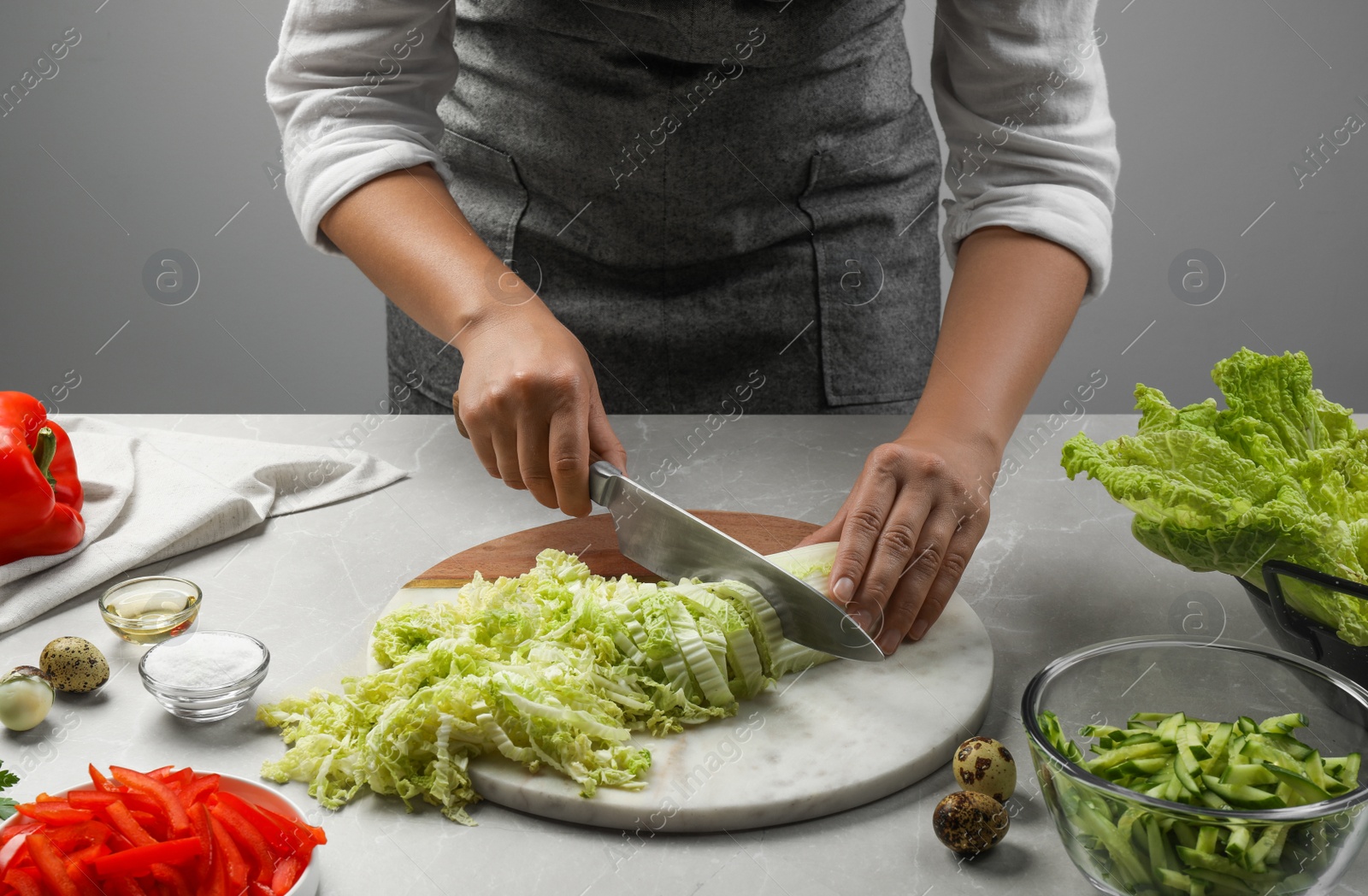 Photo of Woman cutting fresh Chinese cabbage at light grey table, closeup