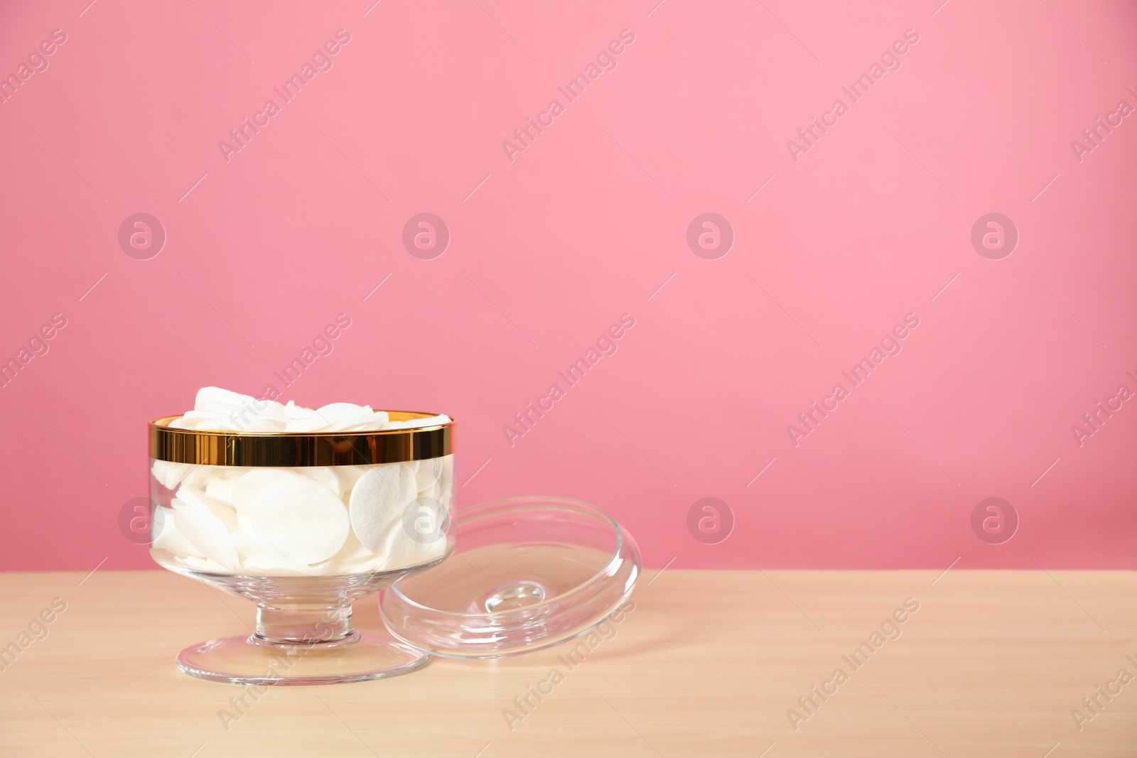 Photo of Jar with cotton pads on wooden table against pink background. Space for text