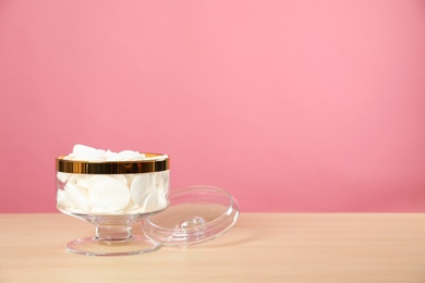Photo of Jar with cotton pads on wooden table against pink background. Space for text