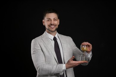 Photo of Happy businessman holding hourglass on black background. Time management