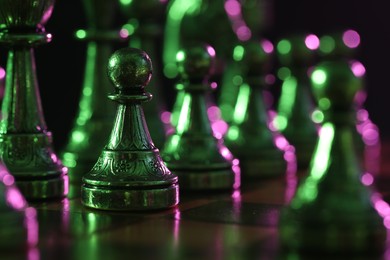 Chess pieces on checkerboard in color light, selective focus