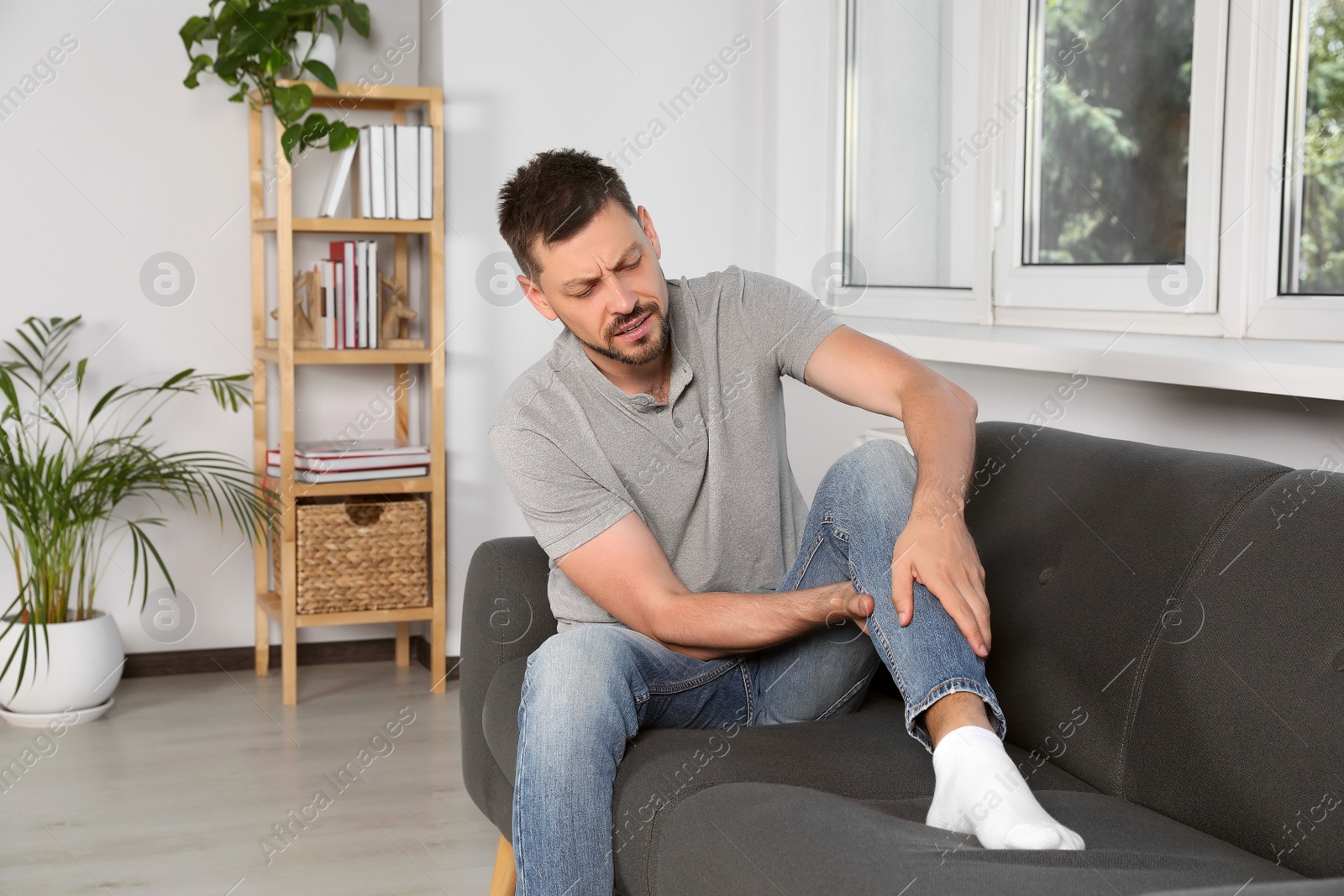 Photo of Man suffering from pain in leg on sofa at home