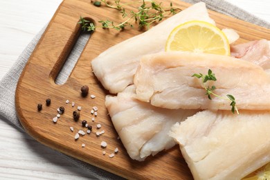 Photo of Pieces of raw cod fish, lemon and spices on white wooden table, above view
