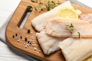 Pieces of raw cod fish, lemon and spices on white wooden table, above view