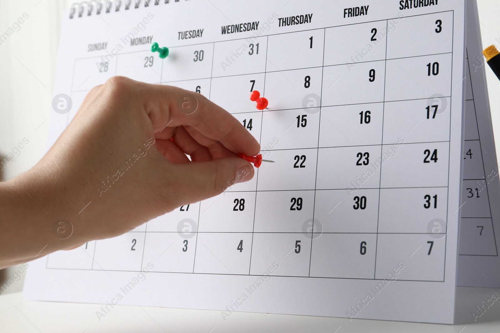 Photo of Timetable. Man marking date in calendar with drawing pins at white table, closeup